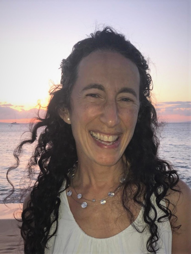 Dr. Carolina Reisenman portrait at a beach with the sunset behind her, smiling.